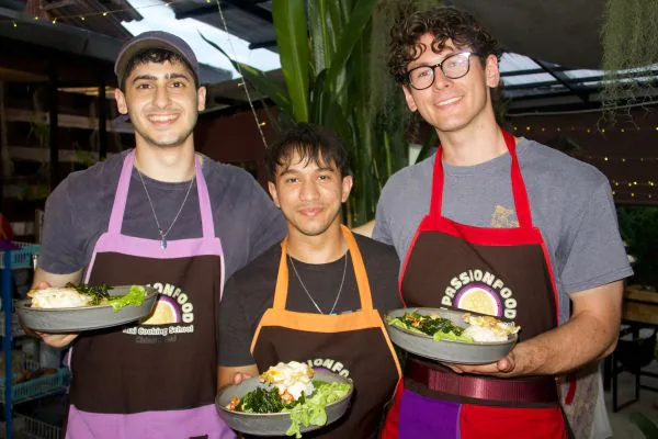 Three students in aprons holding up the plates they cooked