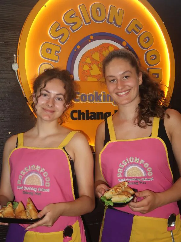 Two guests with their dishes in front of the Passionfood sign, lit up after dark