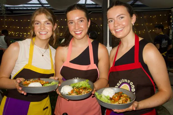 Three students in aprons proudly holding their finished dishes