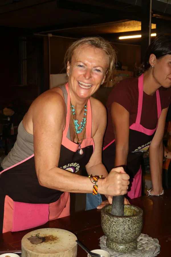 A smiling student pounding curry paste in a stone mortar