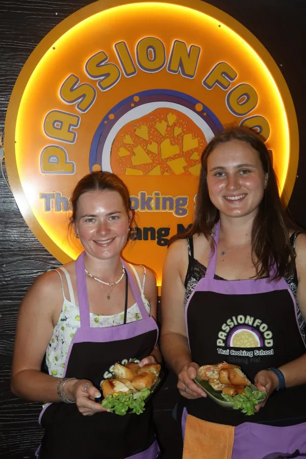 Two students with their dishes in front of the glowing Passionfood sign