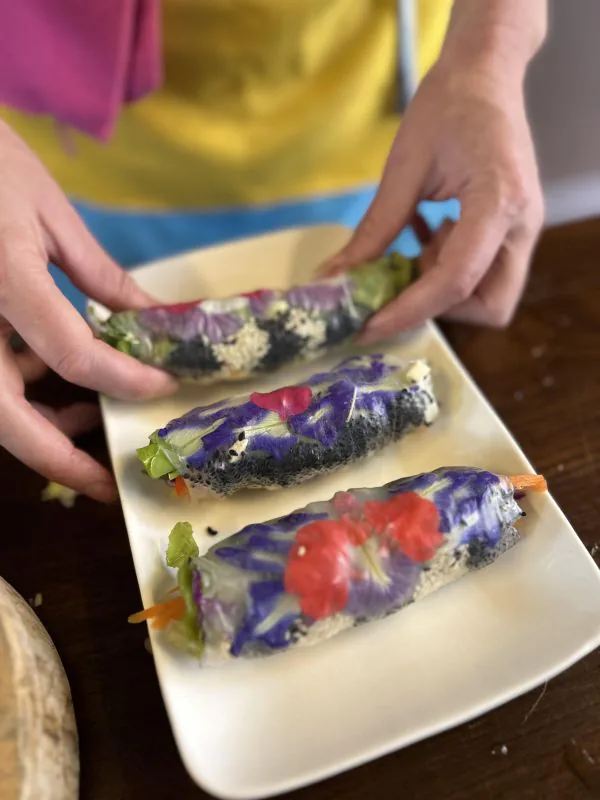 Hands holding a plate of blue-tinted fresh spring rolls